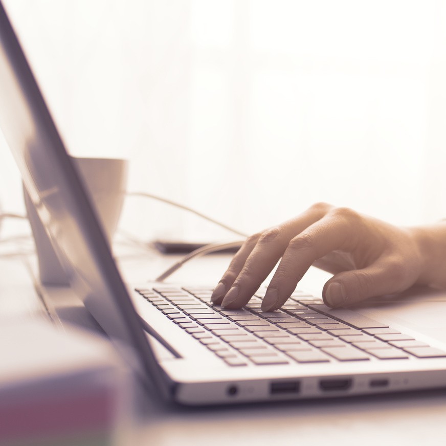 Woman sitting at desk and connecting with her laptop, she is working and typing on the keyboard